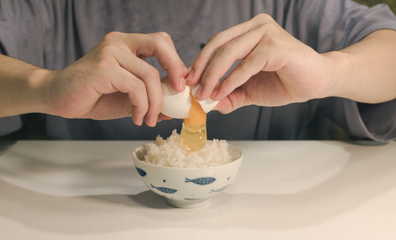 生卵を割って食べる様子と、サルモネラ菌による食中毒リスクを示すイメージ